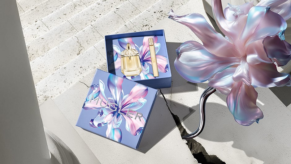 Bannière de la campagne Mugler pour la fête des mères 2026, mettant en scène les flacons emblématiques des parfums Angel et Alien dans un paysage floral céleste et parisien, rendant hommage aux mères extraordinaires.